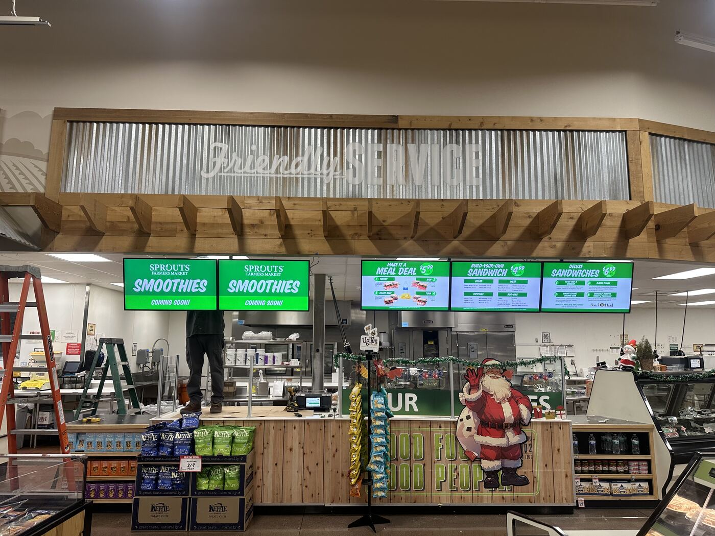 Row of digital menu screens above a grocery store deli counter